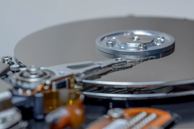 The inside of an opened hard disk drive: a mirror-like platter, the spindle at its center, and the actuator arm reaching across the surface to the read/write head